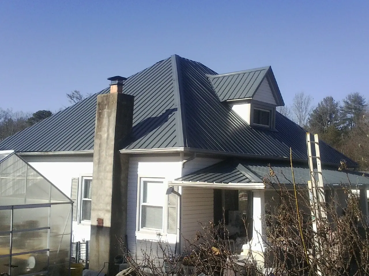 Dark blue standing seam metal roof on a white farmhouse with dormer — Slate & Tile Roof Repair by Roofing Brothers in Foristell