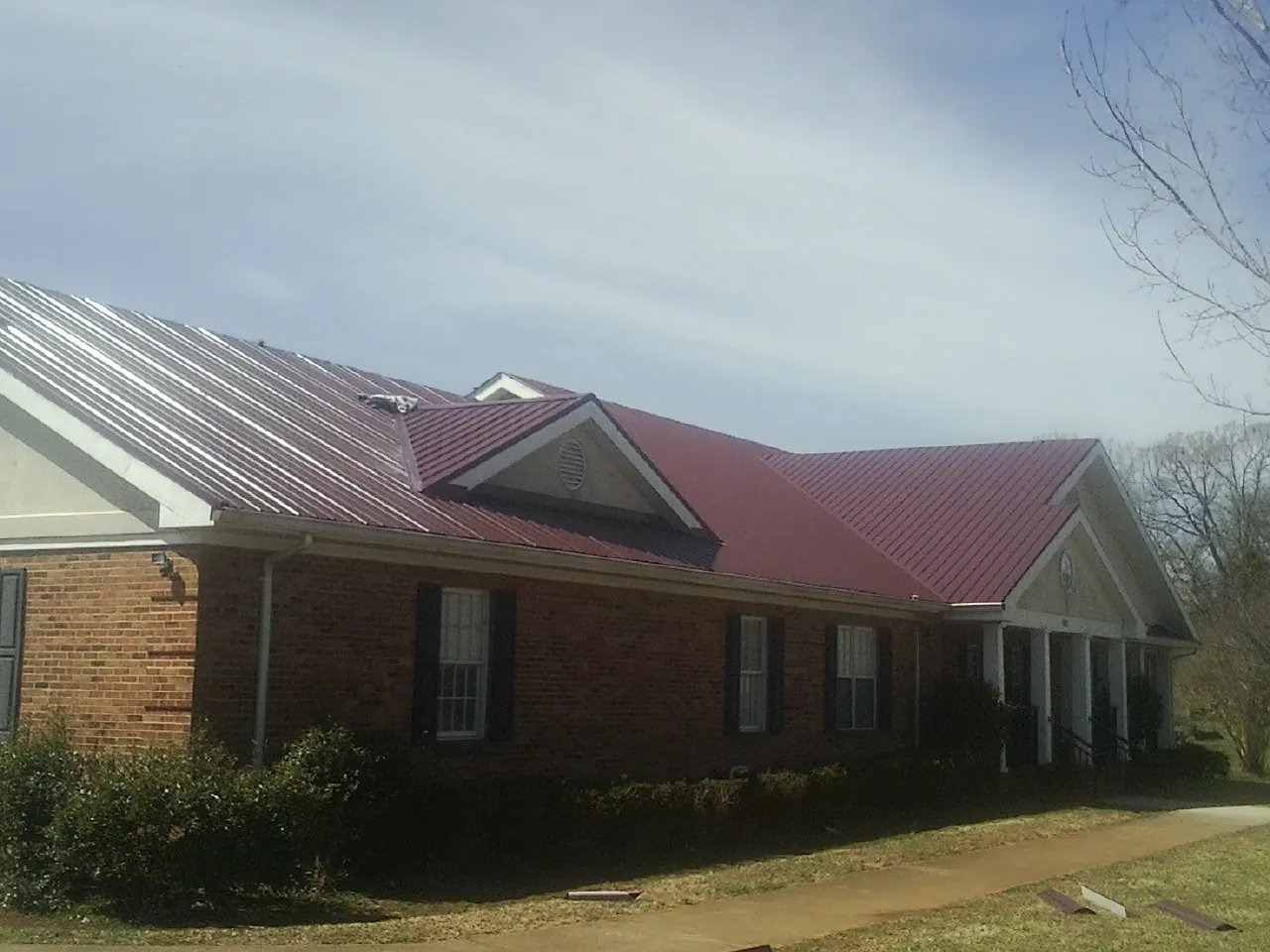 Red metal roof with gabled entries on a long brick building, from a Hail Damage Roof Repair job in Foristell