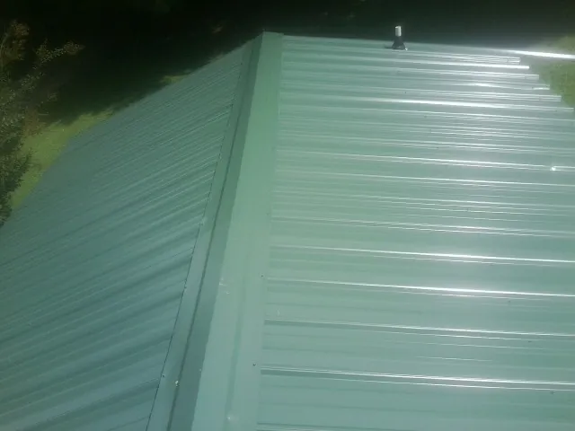 New green metal panels meeting at the ridge of a roof — Flat Roof Repair work by our crew in Foristell